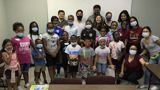 Children and adults wearing face masks gathered together in a community room