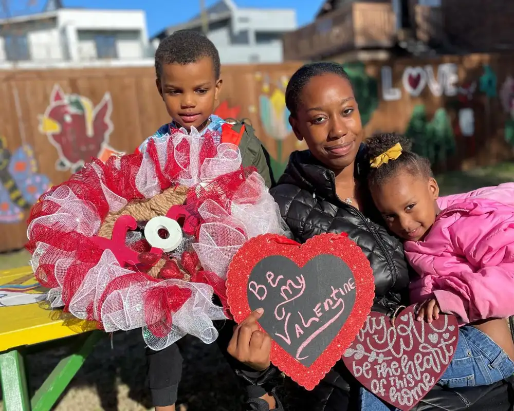 A smiling mother sitting outside with her young son and daughter, holding a handmade valentine heart